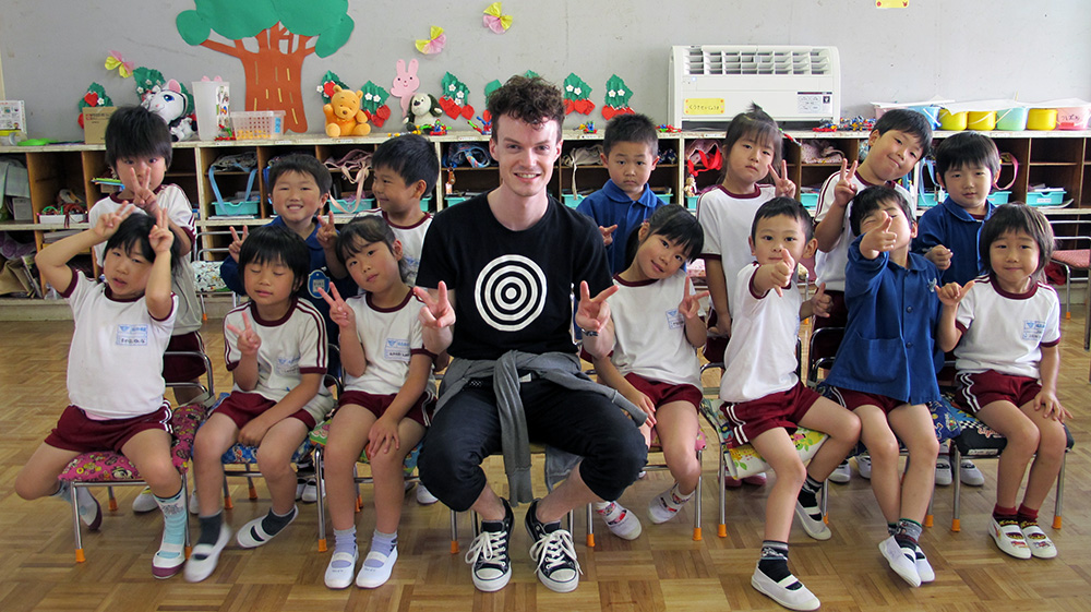 Marcus in a classroom posing with a group of kindergarten-aged pupils