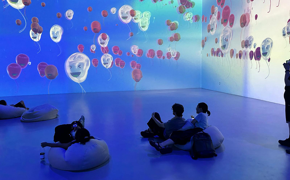 People sitting on beanbags in a gallery were images of ballons are projected on the walls