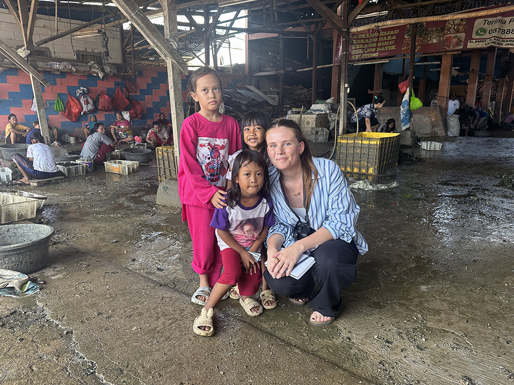 Maddy crouching in a communal space in Timbulsloko with three children